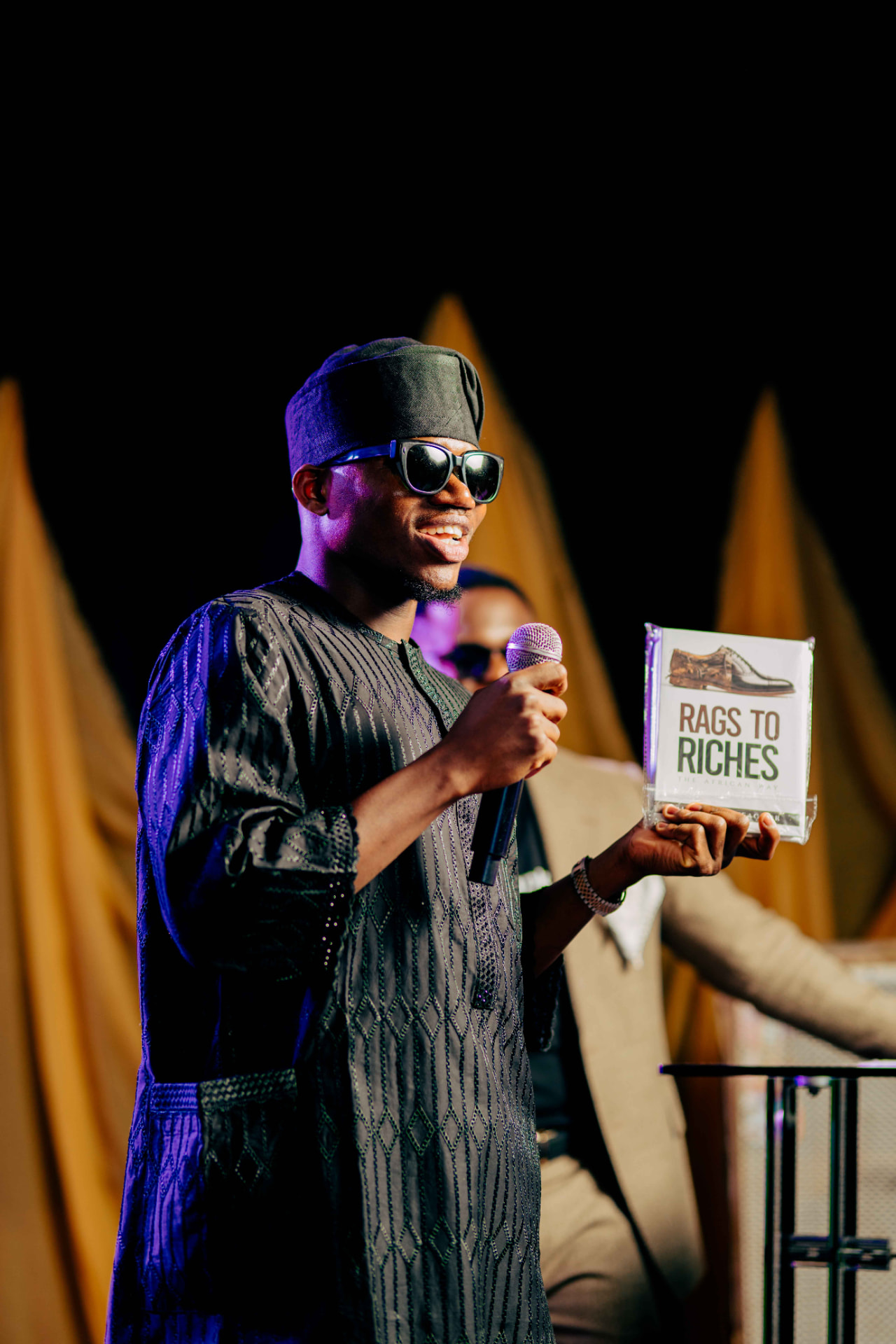 A guest holding up a copy of Rags to Riches on stage