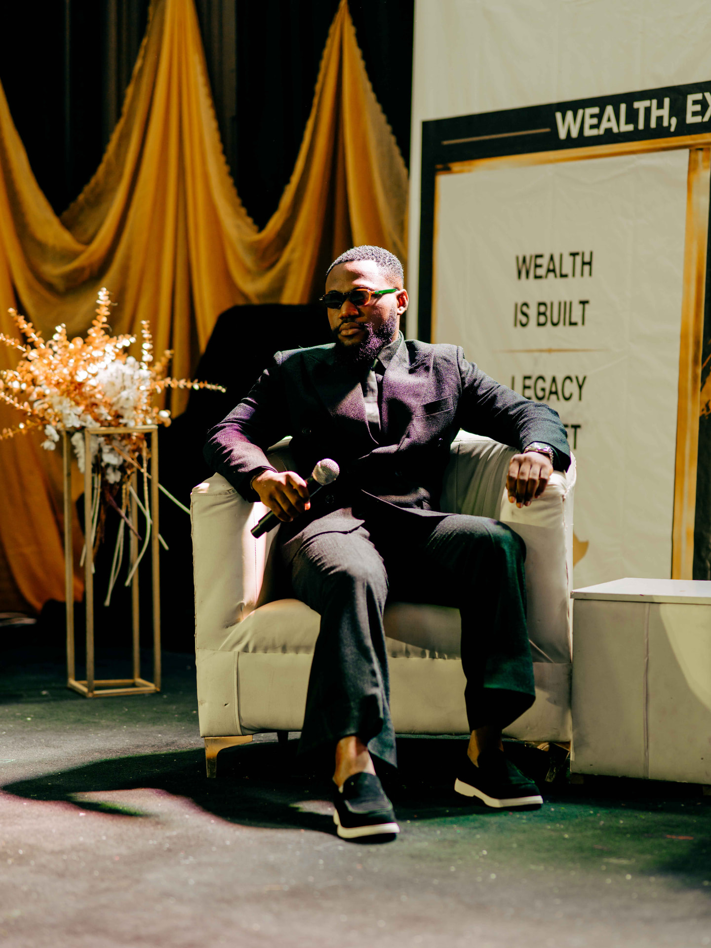 M.N. Onyeachor seated on stage holding a microphone